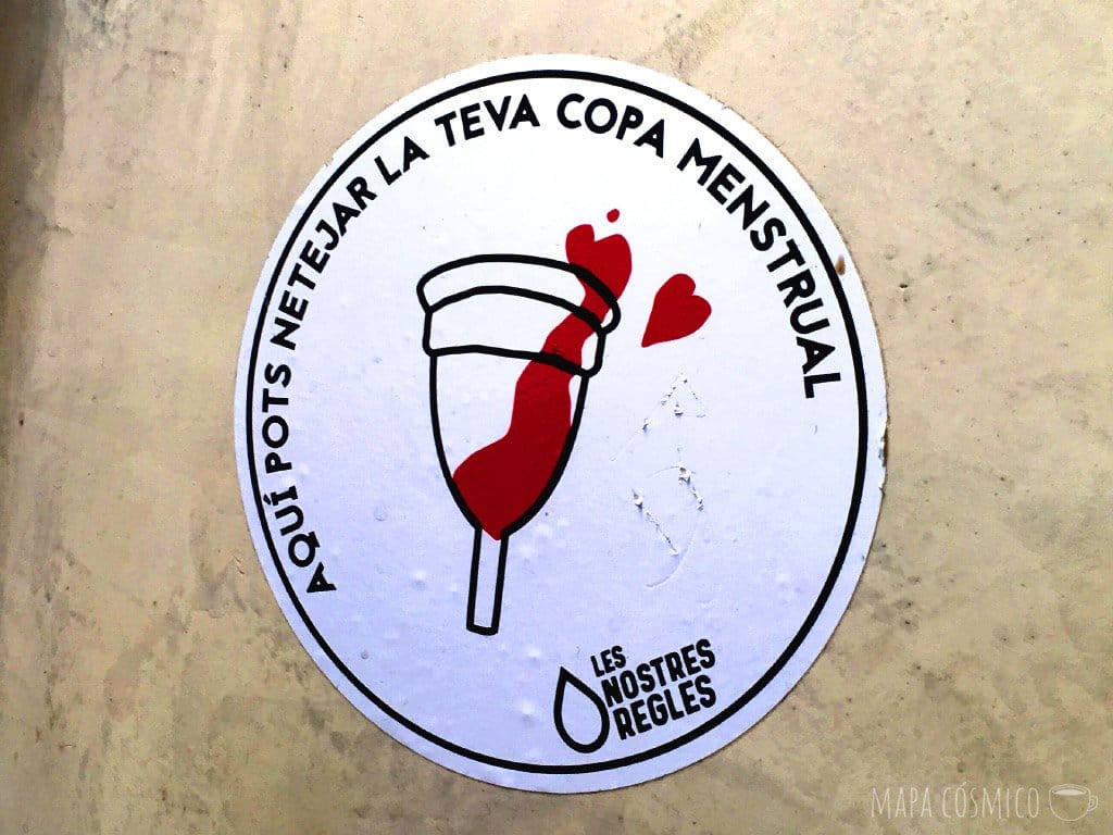 Sticker en un baño catalán, promoviendo el uso de la copa menstrual al viajar, por la agrupación "nuestras reglas"